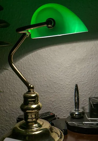 banker's lamp: a distinctive type of desklamp, usually with a solid ornate base and a single stem leading to a...