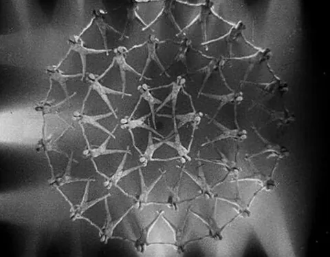 berkleyesque: in the choreographic style of Busby Berkley, involving elaborate geometric patterns creating a...