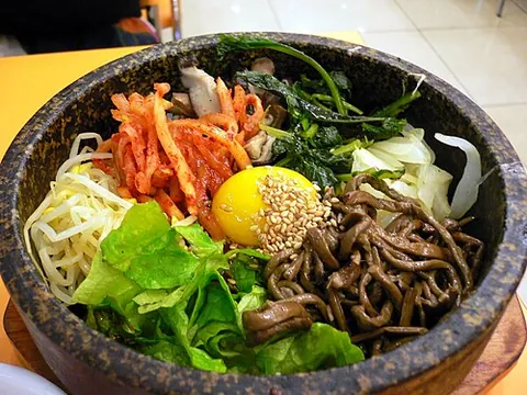 bibimbap: a Korean dish of white rice topped with vegetables, beef, a whole egg, and gochujang (chili pepper...