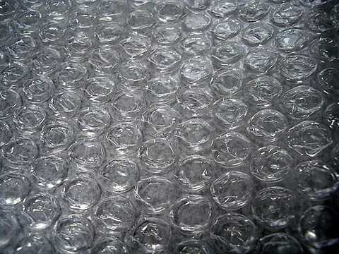 bubble wrap: cushioning material consisting of small spheres of air trapped in plastic, sold on long rolls for...