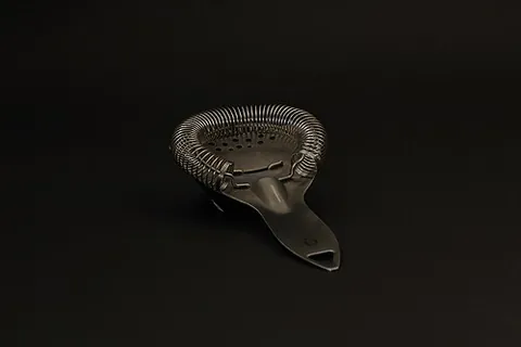 cocktail strainer: a metal bar accessory used to strain mixed drinks as they are poured from the shaker or mixing...