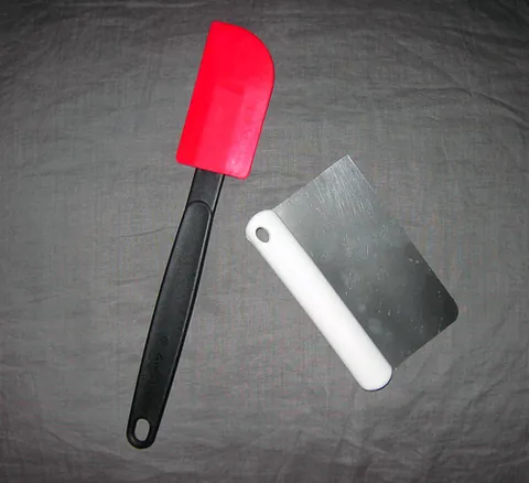 dough scraper: a rubber or metal implement used to scrape food, such as dough, off a countertop, out of a bowl, etc