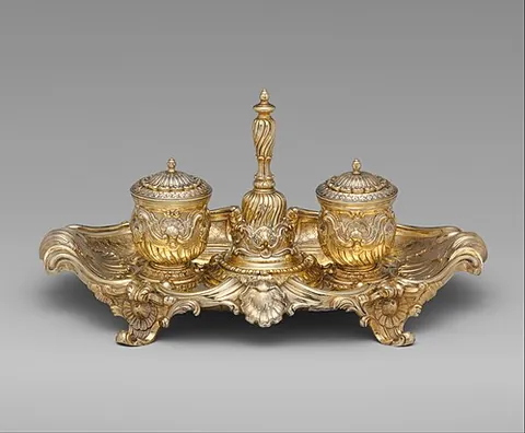 inkstand: a small tray containing pens and an inkwell; (by extension) a pot for holding ink, inkpot, inkwell