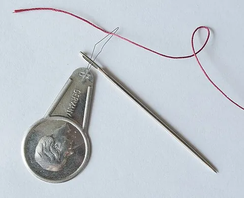needle threader: a device for pulling a thread through the small eye of a needle