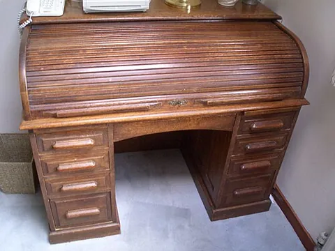 roll-top desk: a desk having a flexible top, made of parallel slats, that rolls away when not needed