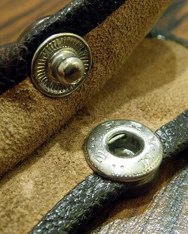 snap fastener: a pair of male/female interlocking disks used to fasten a piece of clothing in place of buttons
