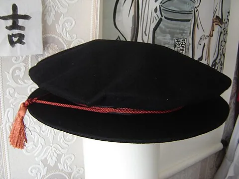tudor bonnet: a traditional soft-crowned, round-brimmed cap with a tassel hanging from an encircling cord,...