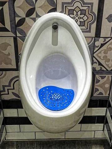 urinal screen: a mesh placed above a urinal's drain to prevent debris from clogging the plumbing, sometimes shaped...