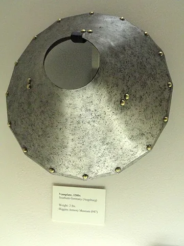 vamplate: a round of iron on the shaft of a tilting lance, to stabilize and protect the hand