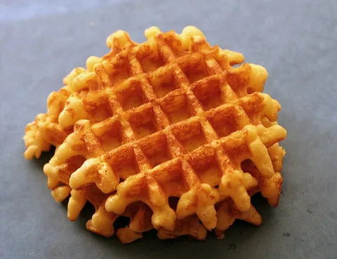 waffle: a flat pastry pressed with a grid pattern, often eaten hot with butter and/or honey or syrup